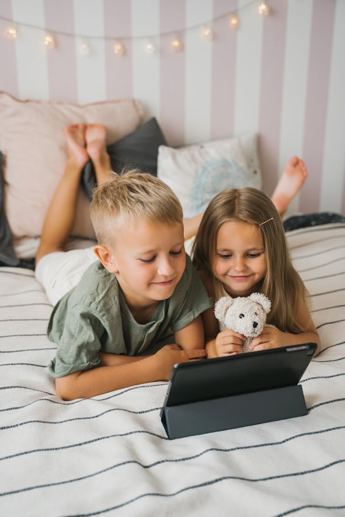 Two children relaxing on a bed while enjoying content on a tablet, creating a cozy atmosphere.