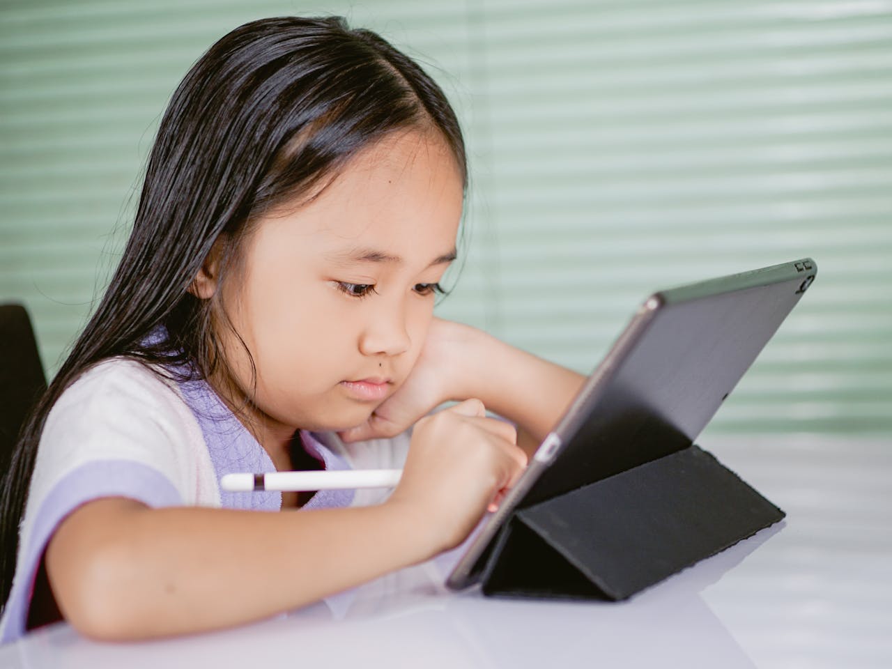 Startseite A young girl using a tablet for online learning, focused and engaged with her digital pen.