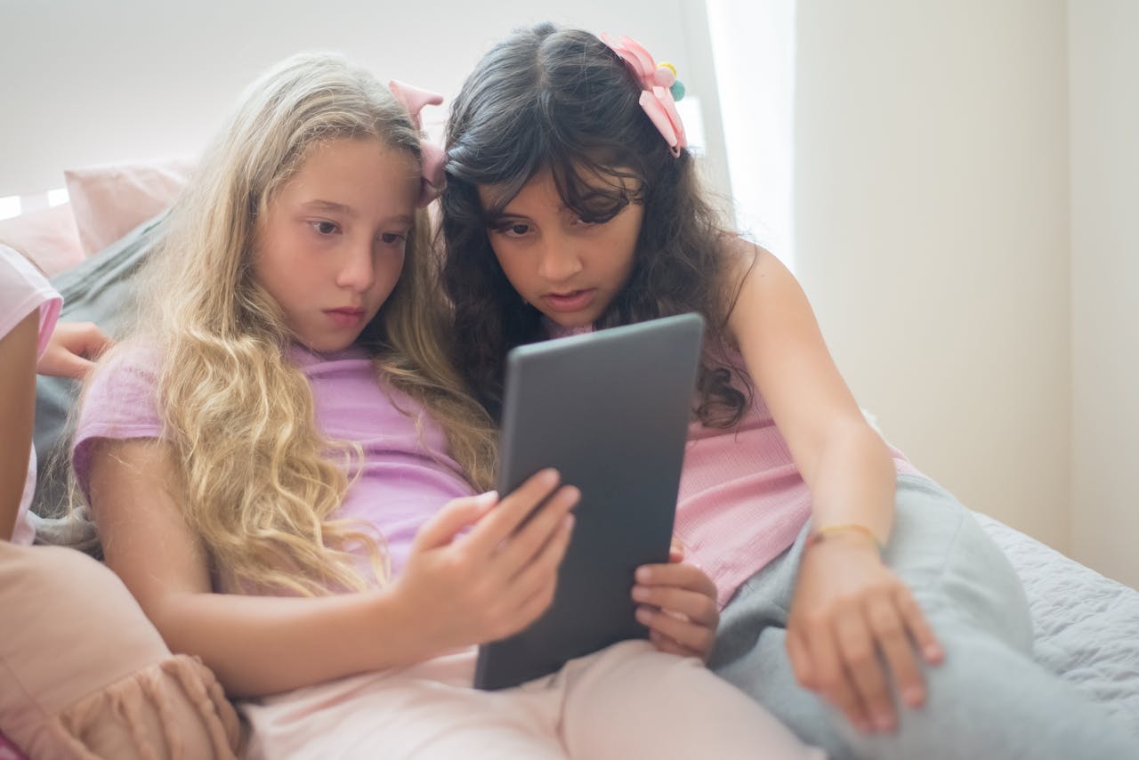 Startseite Two young girls in pajamas using a tablet on a bed, enjoying a digital experience indoors.